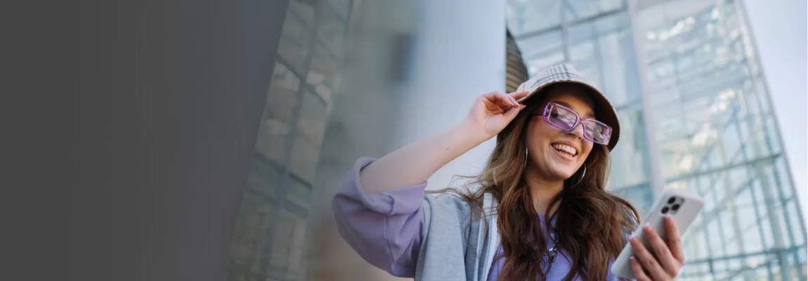 Smiling woman in stylish outfit and sunglasses looking at her smartphone.
